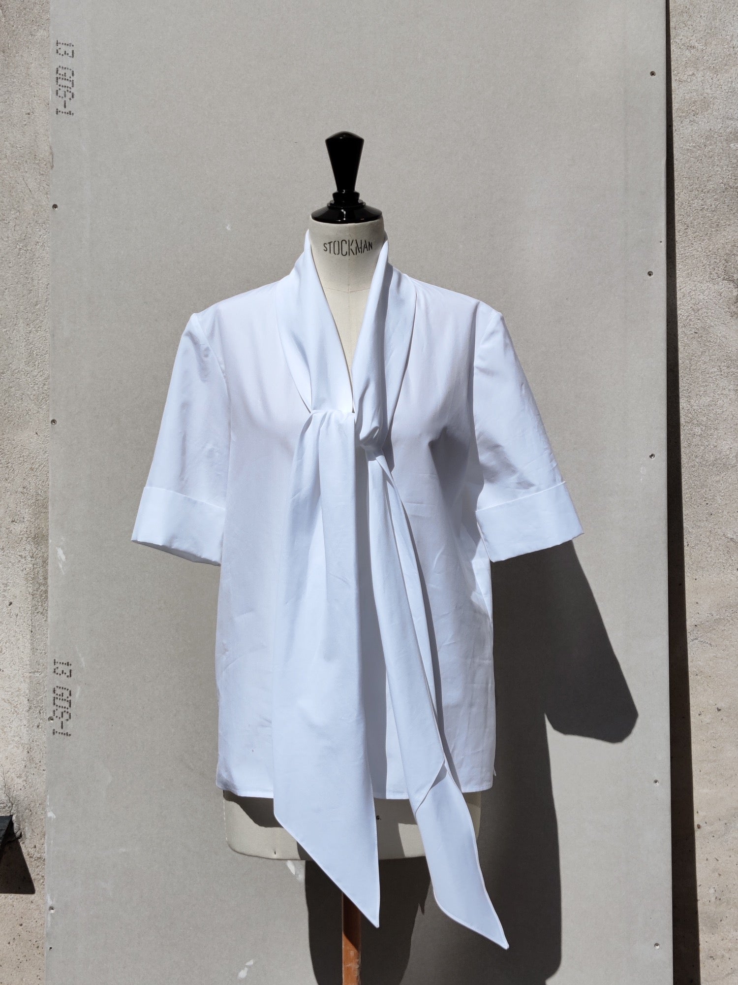 Front view. Alan shirt (white) has a V-shaped neckline incorporating a long ties which can be tied in a knot or a bow or just left.