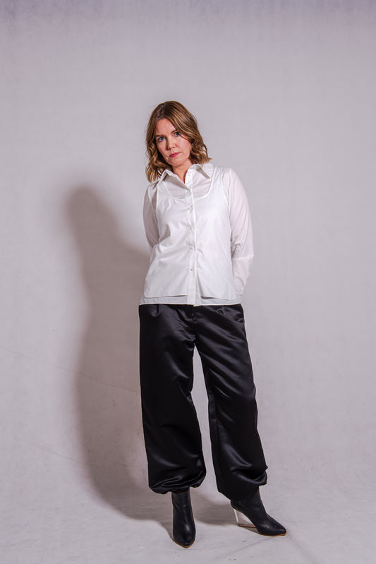 Women wearing Abbey shirt white paired with Agnes trousers (black) against a grey wall.