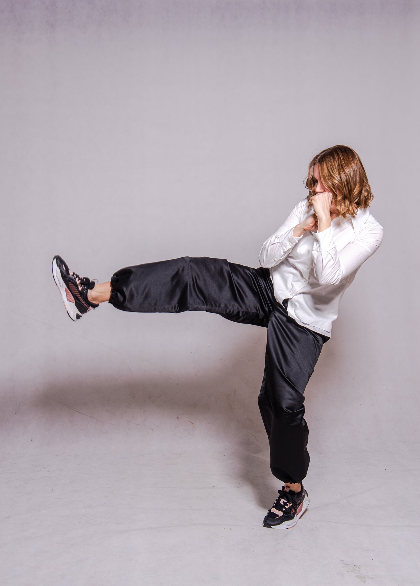 Women wearing Abbey shirt white paired with Agnes trousers (black) against a grey wall.