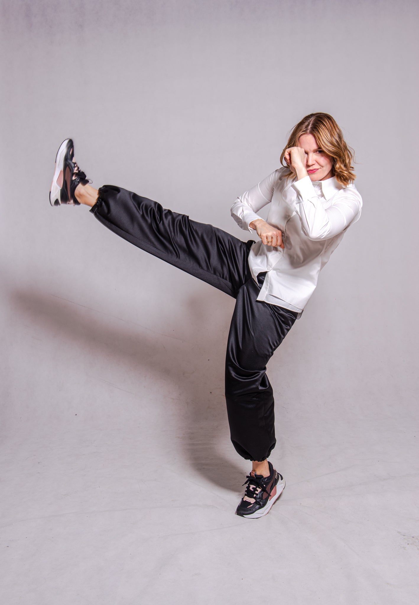 Women wearing Abbey shirt white paired with Agnes trousers (black) against a grey wall.