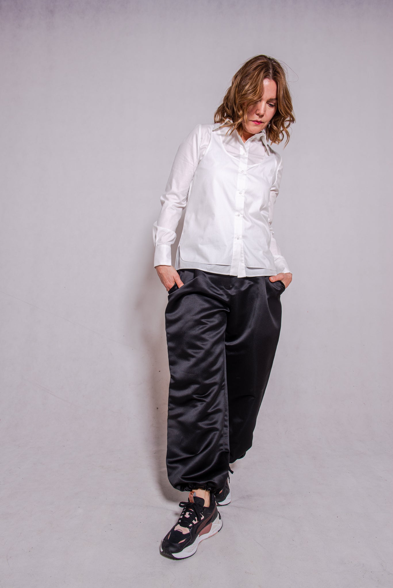 Women wearing Abbey shirt white paired with Agnes trousers (black) against a grey wall.