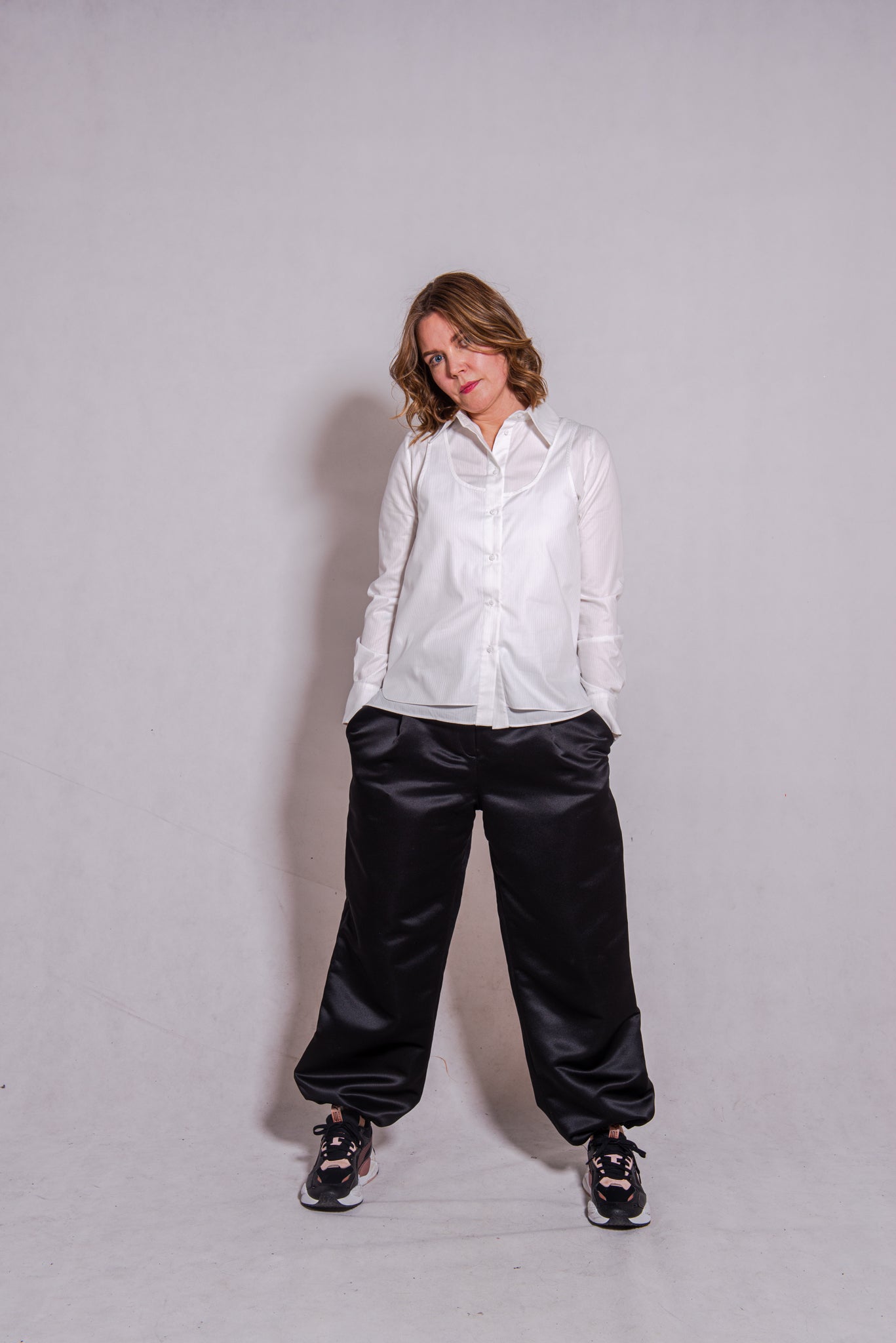 Women wearing Abbey shirt white paired with Agnes trousers (black) against a grey wall.