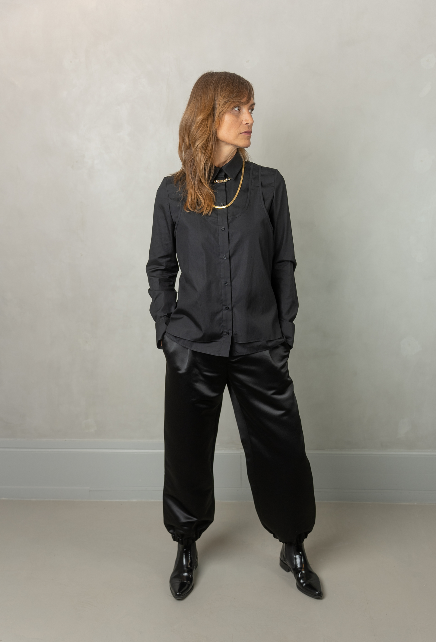 Women wearing Abbey shirt black paired with Agnes trousers (black) against a grey wall.