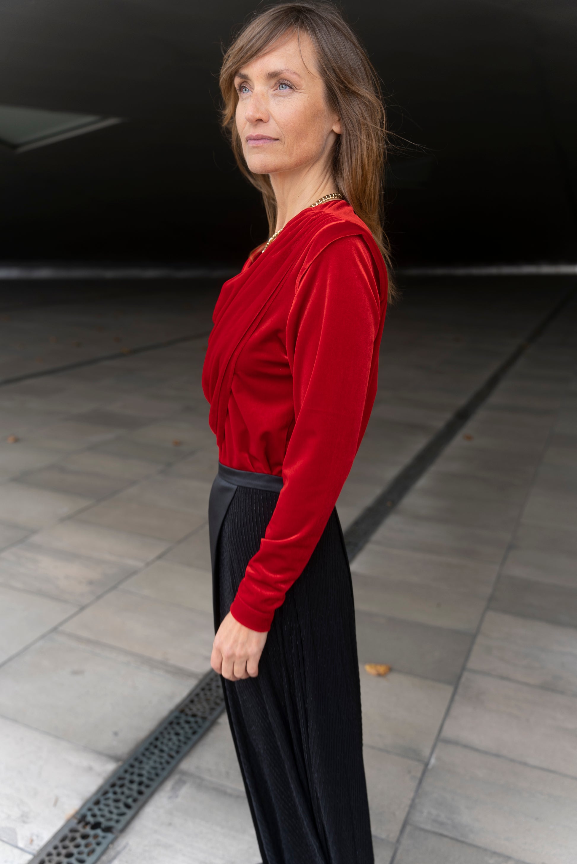 Model wearing Alek top red velvet and Aya skirt stripey multi side view. Looking away