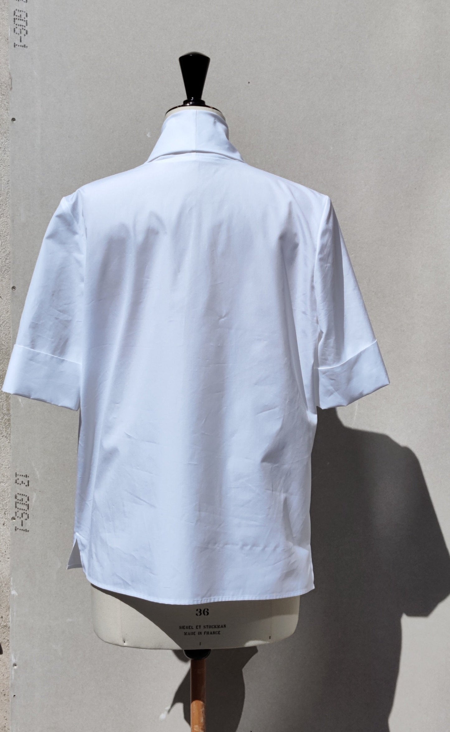 Back view Abba shirt white on a dummy against a grey wall.