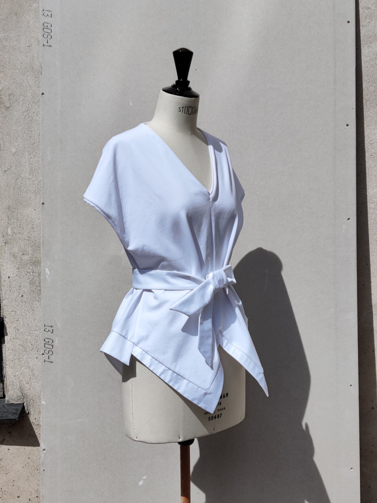 Side view. The Aider top (white) has a handkerchief silhouette and added cotton detail on the hem line.