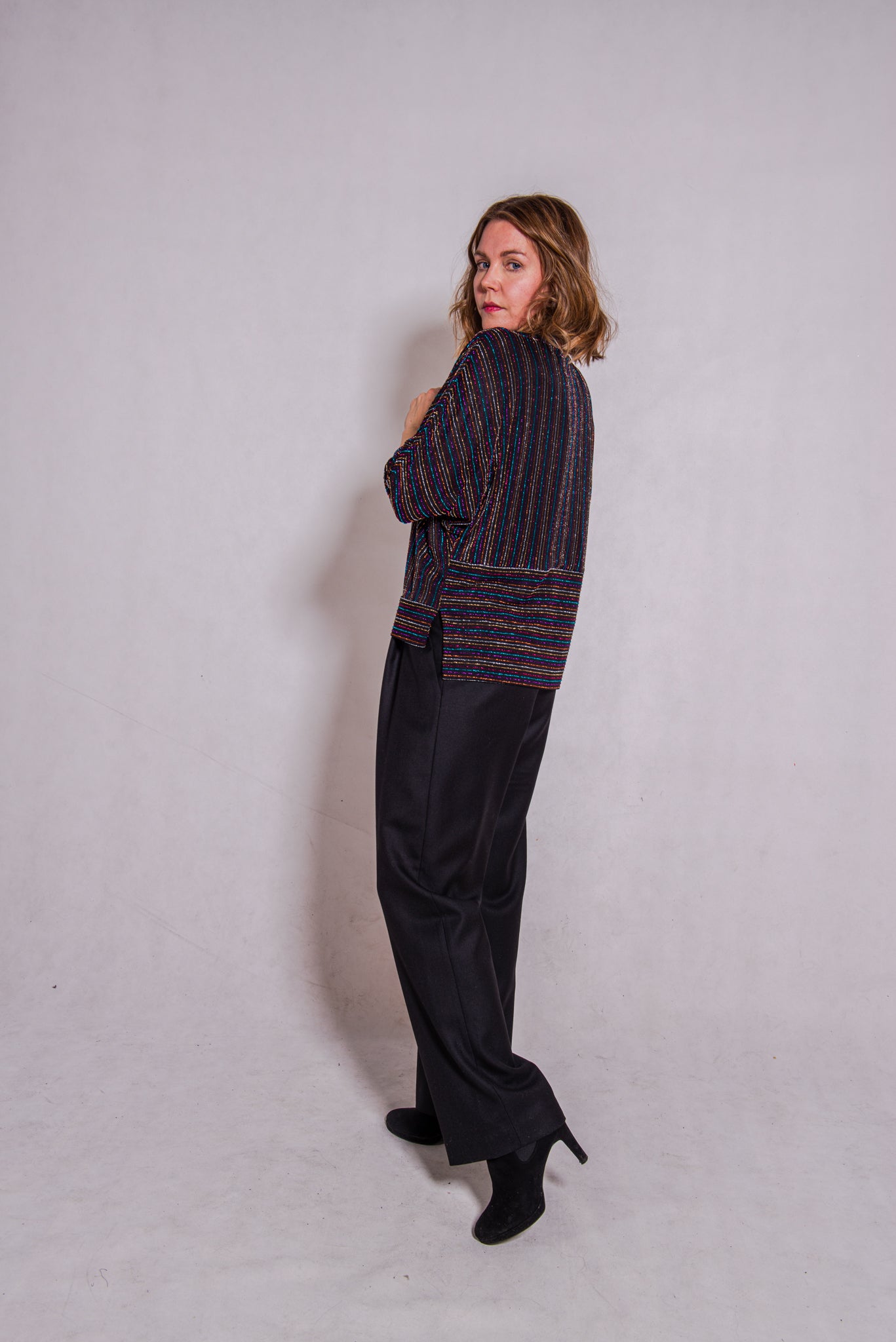 Model, looking back over her left shoulder, wearing Adrianna top, stripey multi & Ava trousers, black.