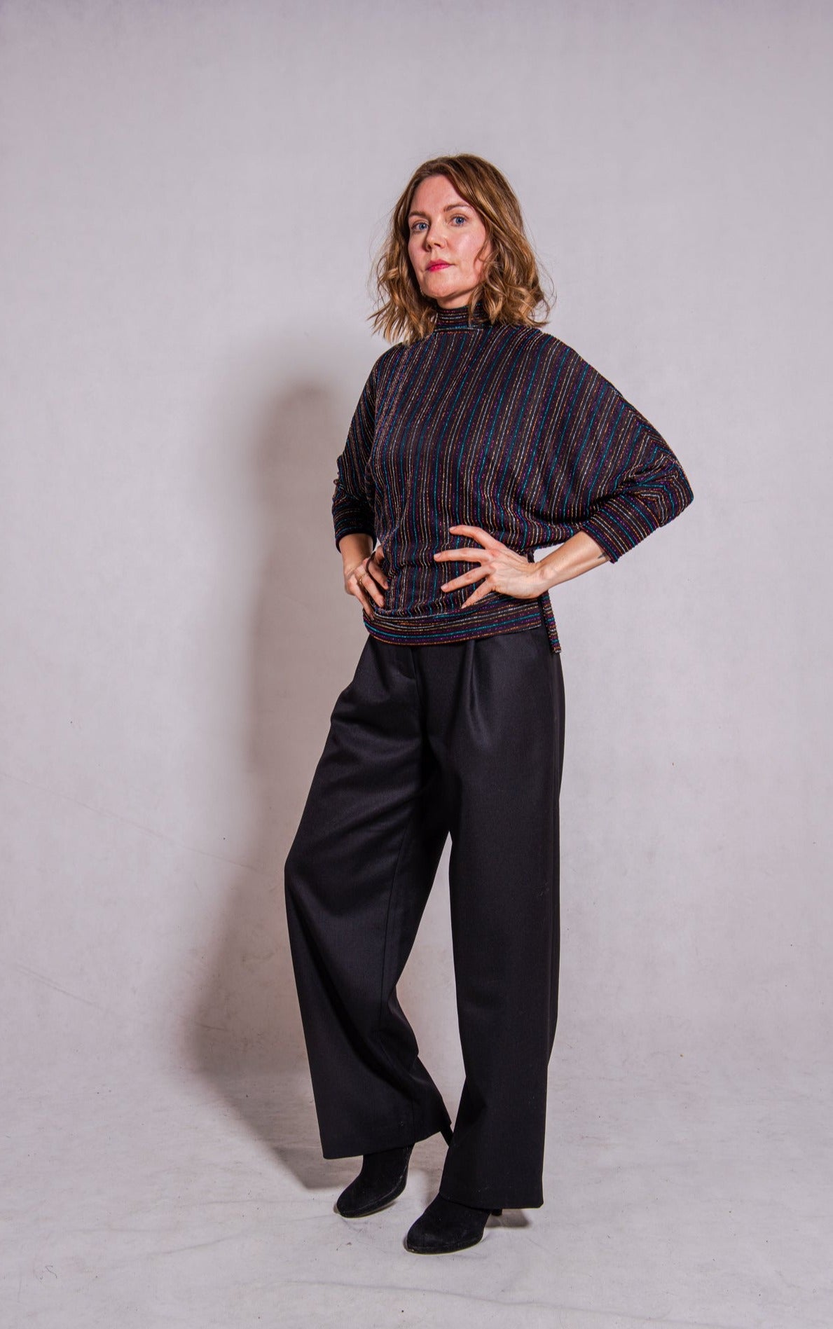 Model, looking direct, wearing Adrianna top, stripey multi & Ava trousers, black. Side view.