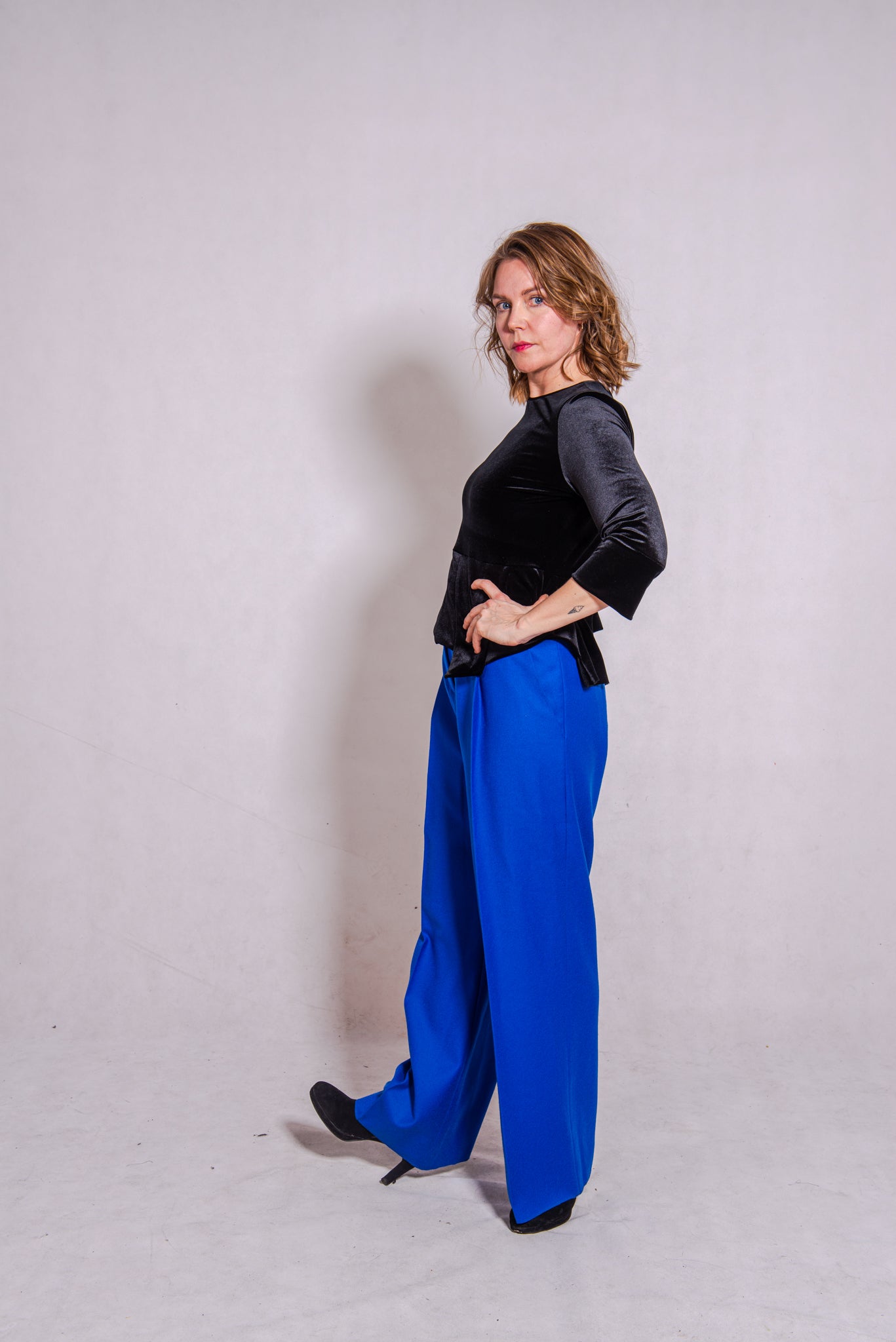 Model looking direct wearing Ann-Marie top, black, & Ava trousers, blue wool..